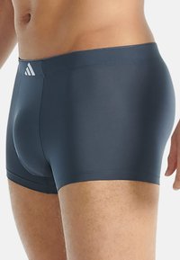 Mäns mörkgrå badbyxor gjorda av ett mjukt, elastiskt material. Har en figurnära design och en liten vit logotyp på midjebandet.