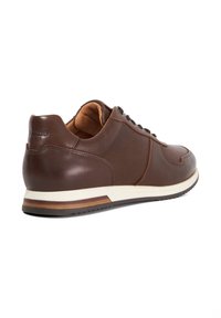 Brown leather sneaker with a perforated design, round toe, lace-up closure, and a contrasting white sole with wooden accents.