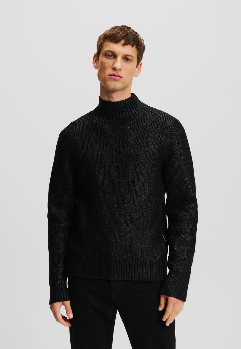 Sort strikket sweater med en høj ribbet krave, prydet med et struktureret diamantmønster. Ribbet manchetter og kant giver et tætsiddende udseende.
