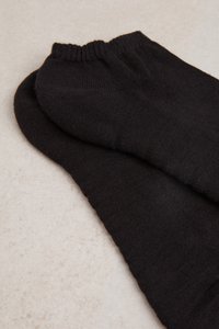 Schwarze Baumwollsocken mit einer glatten Textur, die über einen gerippten Bündchen verfügen. Die Socken liegen flach auf einer hellen Oberfläche.