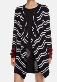 Cardigan lavorato a maglia con un motivo ondulato in bianco e nero, apertura frontale, e strisce rosse sulle maniche; tessuto leggero e strutturato.