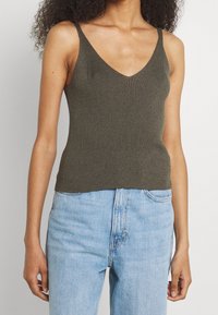 Oliwkowy żeński top na ramiączkach z dekoltem w kształcie V, z cienkimi ramiączkami i dopasowanym krojem, w połączeniu z jasnoniebieskimi jeansami o wysokim stanie.