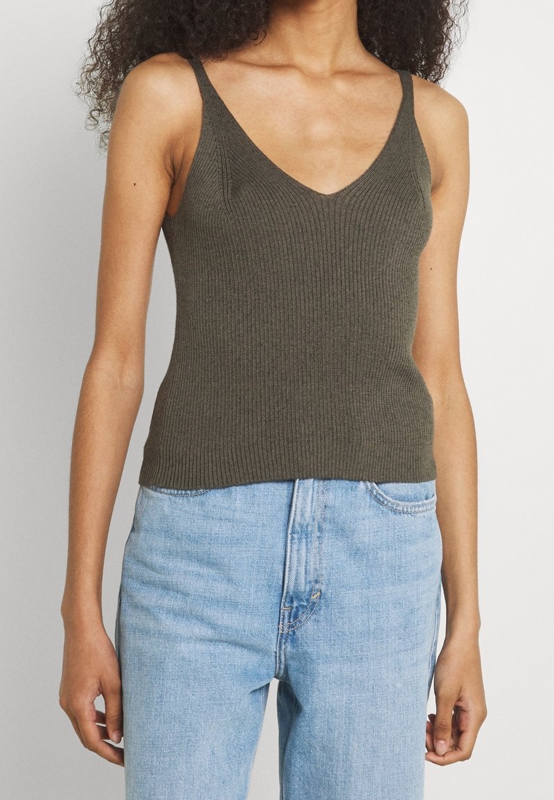 Oliwkowy żeński top na ramiączkach z dekoltem w kształcie V, z cienkimi ramiączkami i dopasowanym krojem, w połączeniu z jasnoniebieskimi jeansami o wysokim stanie.