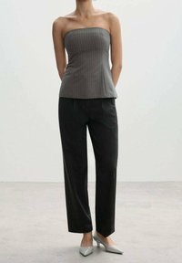Haut gris sans bretelles à fines rayures associé à un pantalon sombre sur mesure et des escarpins gris clair à bout pointu. Tissu lisse et silhouette structurée.