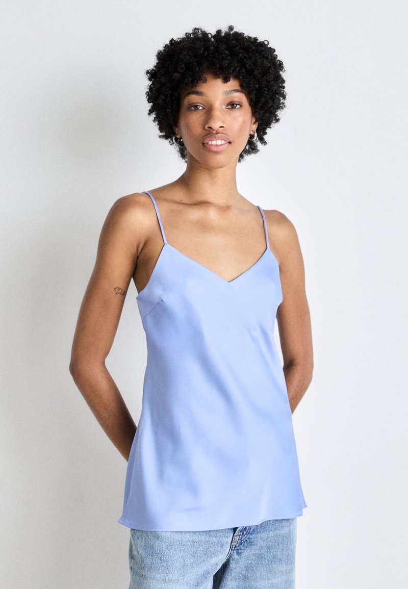 Camisole de satin albastru deschis cu bretele subțiri ajustabile, guler în V și o textură netedă, asortat cu blugi din denim albastru.