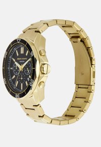 Kuldse tooni roostevabast terasest kell musta lillemustriga, hõbedaste tunnimarkerite, kroonograafi alamdialoogide ja kolme lingiga käevõru disainiga.