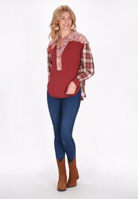 Top a maniche lunghe con corpo bordeaux e spalle a motivo floreale, abbinato a maniche scozzesi, indossato con jeans skinny blu e stivali marroni.