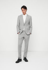 Fato cinza-claro com um blazer ajustado e calças a condizer, apresentando uma textura suave e uma camisa branca imaculada. Sapatos sociais pretos completam o visual.