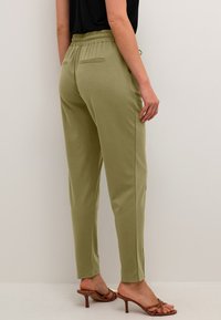 Olivno zelene meke jogger hlače z elastičnim pasom, stranskimi žepi in zoženimi nogami, v kombinaciji s brownimi visokimi sandali.