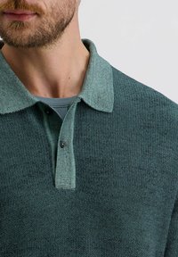 Kragenpullover in dunkelgrün mit strukturiertem Strick, ausgestattet mit einem kontrastierenden hellgrünen Kragen mit zwei Knöpfen und einer glatten Innenschicht.