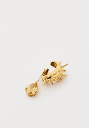 Gold ear cuff with multiple spikes and a dangling teardrop-shaped yellow gemstone on a plain white background.