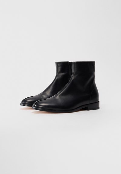 Paar schwarze Leder-Stiefeletten mit Seitenreißverschlüssen und geteilter Zehenpartie, auf einem schlichten weißen Hintergrund abgebildet.