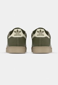 Sneakers in suede verde con dettagli beige, dotate di collo imbottito, suola in gomma e logo distintivo Adidas sul tallone.
