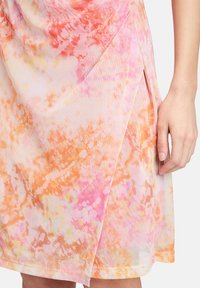 Une robe tie-dye rose et orange avec une texture douce, une coupe asymétrique et une fente sur le côté pour plus de détails.