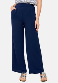 Námořnické široké kalhoty vyrobené z lehkého materiálu s hladkým povrchem. Obsahují přední kapsy a plochý pas. Stříbrné sandály dotvářejí vzhled.