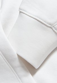 Sweatshirt de algodón blanco con puños texturizados. El material es suave, con un acabado liso y costuras sutiles que le dan un aspecto limpio.