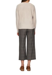 Suéter beige claro con dobladillo acanalado, combinado con pantalones de cuadros grises de pierna ancha y zapatos marrones. El suéter presenta un diseño simple y clásico.