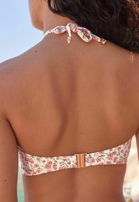 Ziedu raksts bikini tops ar gaišu fonu, ar mezglu saišu unmetālisku sprādzi aizmugurē drošai un ērtai piestiprināšanai.