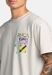 Lichtgrijze T-shirt met korte mouwen, voorzien van kleurrijke grafische prints inclusief tekst, een skelet en geometrische vormen op de voorkant.
