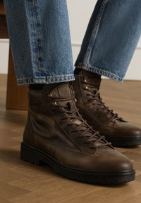 Bruine leren veterschoenen met een gestructureerd oppervlak, ronde neus en contrasterende zwarte rubberen zolen, gecombineerd met lichtblauwe denimjeans.
