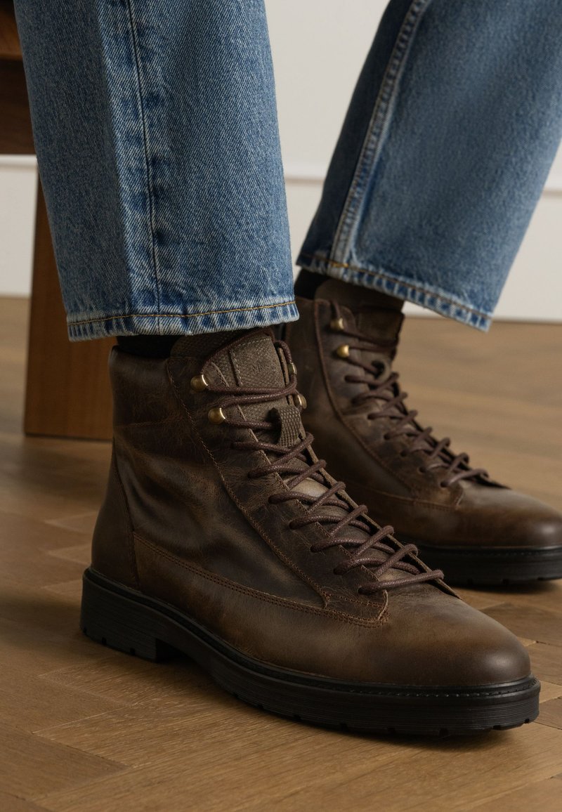 Bruine leren veterschoenen met een gestructureerd oppervlak, ronde neus en contrasterende zwarte rubberen zolen, gecombineerd met lichtblauwe denimjeans.