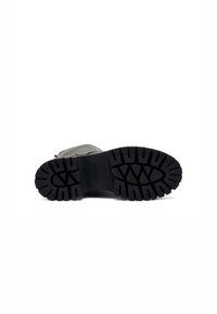 Suela de bota de goma negra con profundas ranuras, un logo estampado y un diseño robusto que mejora la tracción y la durabilidad.
