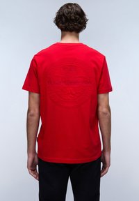 T-shirt in cotone rosso con un logo circolare testurizzato sul retro. Maniche corte e vestibilità rilassata, con orlo dritto.