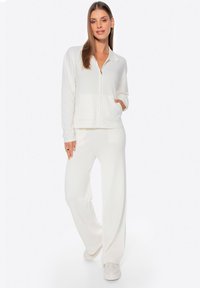 Chaqueta blanca con cremallera, cuello y bolsillos frontales, combinada con pantalones de pierna ancha a juego. Tejido suave con un acabado texturizado.