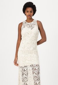 Kanten jurk in off-white met een mouwloos ontwerp, met bloempatronen en een semi-doorzichtig onderste gedeelte. Gelaagd haakwerk materiaal.