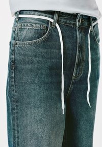 Dunkelblaue Denim-Jeans haben eine lockere Passform und eine weiße Kordelzugakzent. Die Textur ist leicht abgenutzt, mit sichtbaren Nähdetails.
