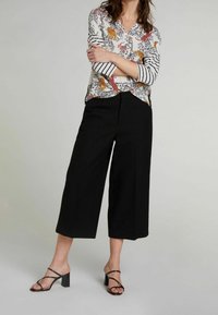 Blusa a fantasia floreale con pantaloni larghi neri e sandali con tacco a strappo neri. La blusa presenta una combinazione di colori e strisce.