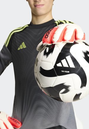 Giovane portiere di calcio con maglia nera e verde tiene un pallone da calcio Adidas bianco e nero con guanti rossi.