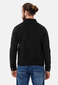 Veste en jean noir avec un col, des poignets boutonnés et une coupe ajustée. Présente un empiècement au dos et des détails de couture subtils. Associée à un jean bleu.
