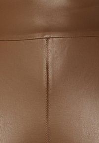 Pantaloni vegani in pelle marrone con una texture liscia. Presentano una cucitura centrale e un design minimalista che mette in risalto la lucentezza del materiale.