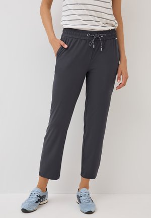 Donkergrijze, lichtgewicht broek met een elastische tailleband en trekkoord; heeft zijzakken en een tapered leg ontwerp. Draagt samen met lichtblauwe sneakers.