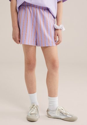 Gyermek, aki levendulalila és narancssárga csíkos rövidnadrágot, fehér zoknit, ezüstszínű sportcipőt, valamint fehér hajgumit visel a csuklóján.