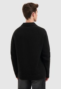 Zwarte fuzzy trui met een gestructureerde stof, lange mouwen en een kraag, met een iets losse pasvorm en een rechte zoom.