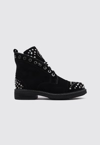 Botines de ante negro con tachuelas plateadas, puntera redonda, ojales de metal y un tacón bajo apilado. Presenta acentos decorativos en la puntera y los laterales.