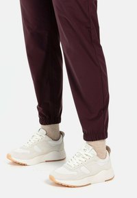 Weiße Sportsneaker aus strukturiertem Stoff mit Schnürsenkeln und einer Gummisohle, kombiniert mit taillierten bordeauxroten Jogginghosen mit elastischen Bündchen.