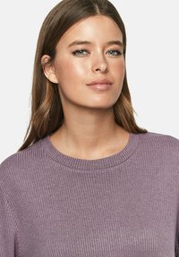 Lichtpaarse geribde trui met een klassieke ronde hals, die een zachte textuur en een aansluitend design toont. Het model heeft lang haar en een neutrale uitstraling.