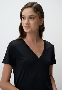 Czarna koszulka typu V-neck z krótkimi rękawami, wykonana z gładkiego materiału. Prosty design bez wzorów lub akcentów, przedstawiająca zbliżenie dekoltu.