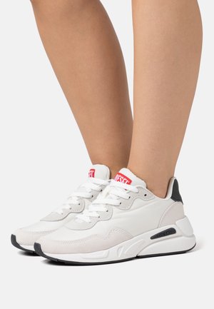 Witte en grijze sportschoenen met een combinatie van leer en suède, voorzien van een rood logo en zwarte accenten op de hiel en zool.