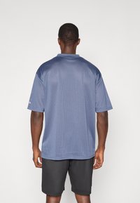 Marinblå kortärmad skjorta med meshstruktur, med polo-krage och lös passform, tillsammans med texturerade svarta shorts.