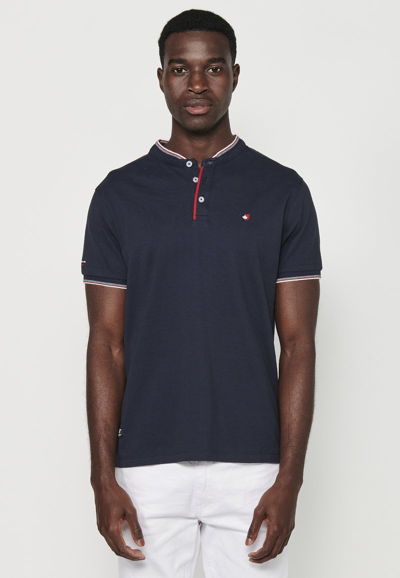 Mornarski polo majica s teksturiranim završetkom, featuring okovratnik, dvostruki gumbasti kopčanje i crveno-bijele naglaske na ovratniku i rukavima.