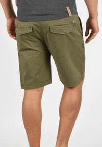 Shorts de color verde oliva hechos de algodón suave, con dos bolsillos traseros, dobladillos cosidos y un corte relajado con una pretina elástica.