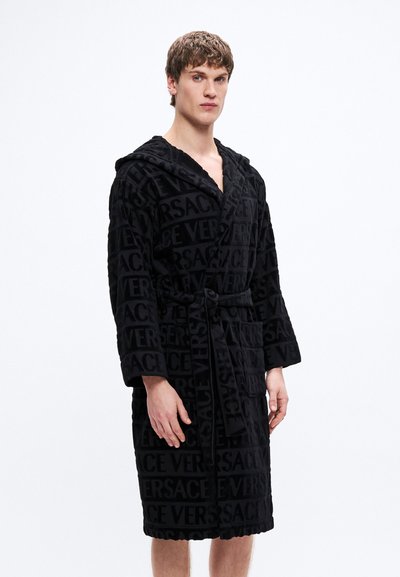 Čierny župan s kapucňou z plyšovej tkaniny, zdobený reliéfnym vzorom s logom Versace. Má pás na stiahnutie v páse a dlhé rukávy.