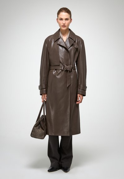 Bruine leren trenchcoat met een ceintuur in de taille, grote revers en lange mouwen. Gecombineerd met grijze broeken en een gestructureerde handtas.
