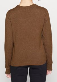 Brauner Pullover mit langen Ärmeln, Rundhalsausschnitt, gerippten Bündchen und Saum sowie einer strukturierten Oberfläche, getragen über einer schwarzen Hose, Ansicht von hinten.