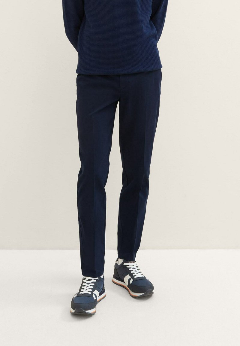 Marinblå byxor med rak skärning, tillverkade av slät tyg. Kombineras med mörka sneakers med vita accenter och en strukturerad design.