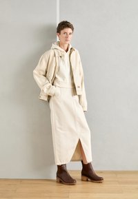 Πετρόλ τζάκετ από τζιν πάνω σε λευκό φούτερ, συνδυασμένο με μια πετρόλ φούστα με μπροστινή σχισμή. Καφέ μποτάκια με χοντρό τακούνι και απλή υφή.